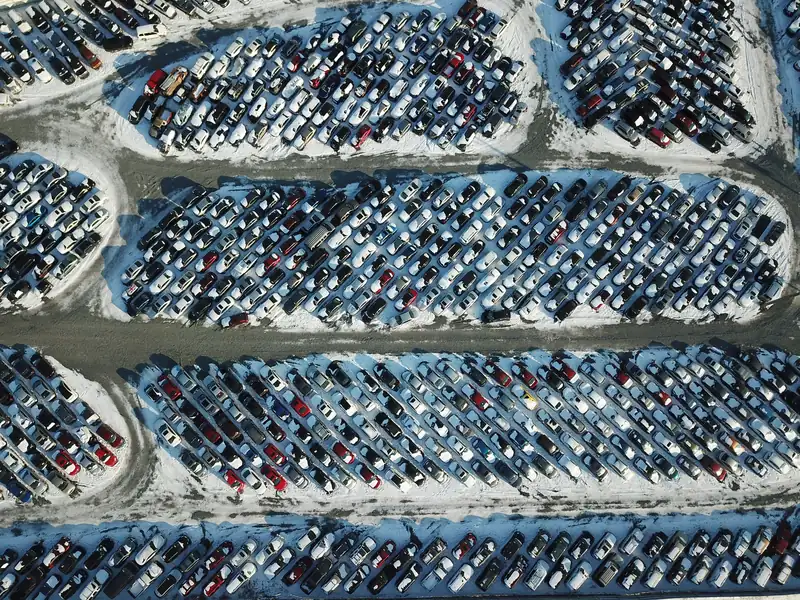 Hundrevis av biler parkert i rader på en snødekt plass, sett ovenfra