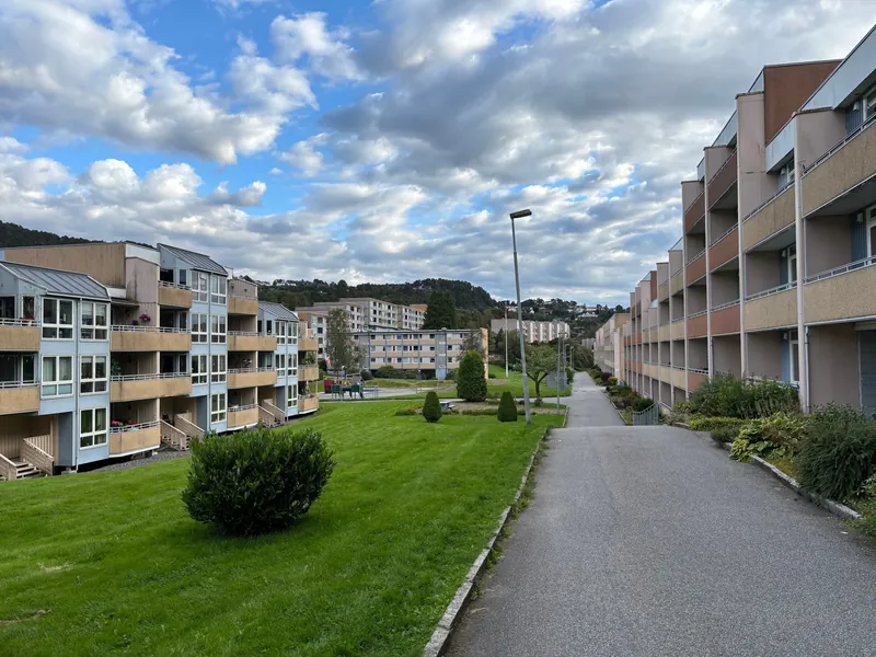 Boligblokker med balkonger langs en gangvei med plen og busker, i Bergen