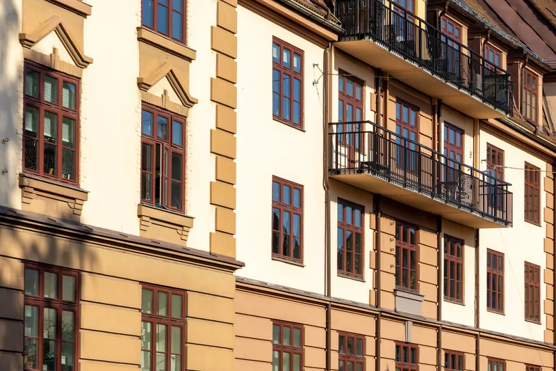 Fasaden på en bygård i Oslo med balkonger og røde vinduer i sollys