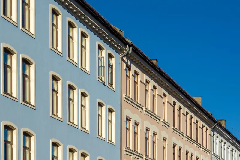 Fasadene på en lyseblå og en beige bygård i Oslo, sett skrått nedenfra mot blå himmel