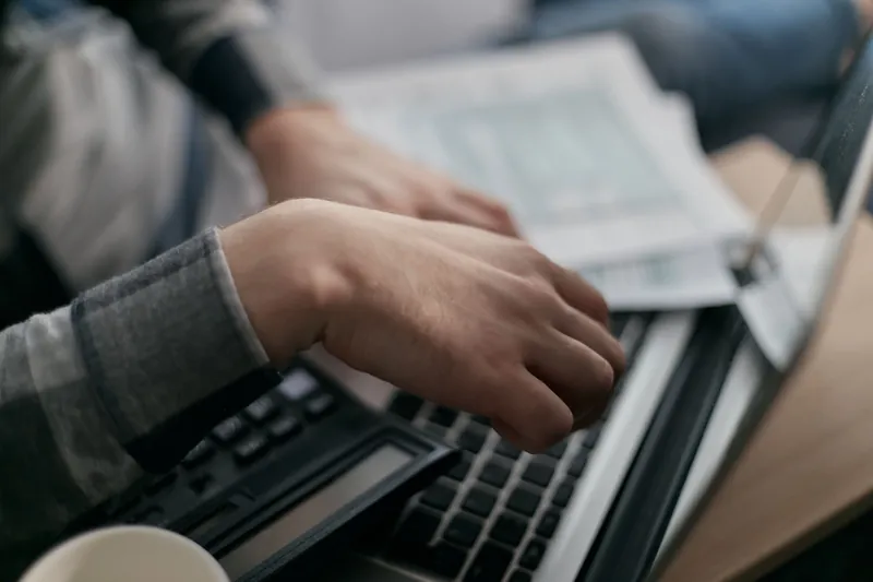 Hender over et tastatur og en kalkulator, med papirer ute av fokus i bakgrunnen