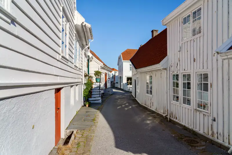 Hvite trehus med røde tak langs en smal, brolagt gate en solskinnsdag