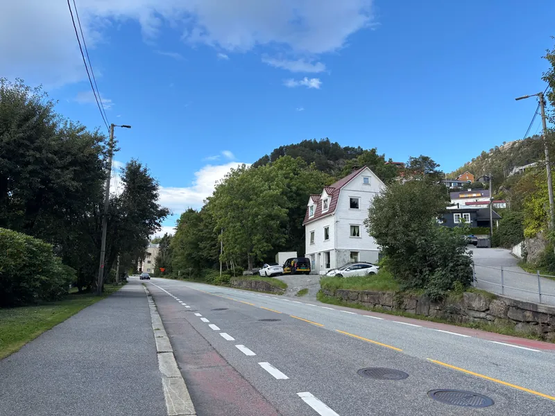 Et hvitt trehus med rødt tak ved en vei i et norsk boligstrøk
