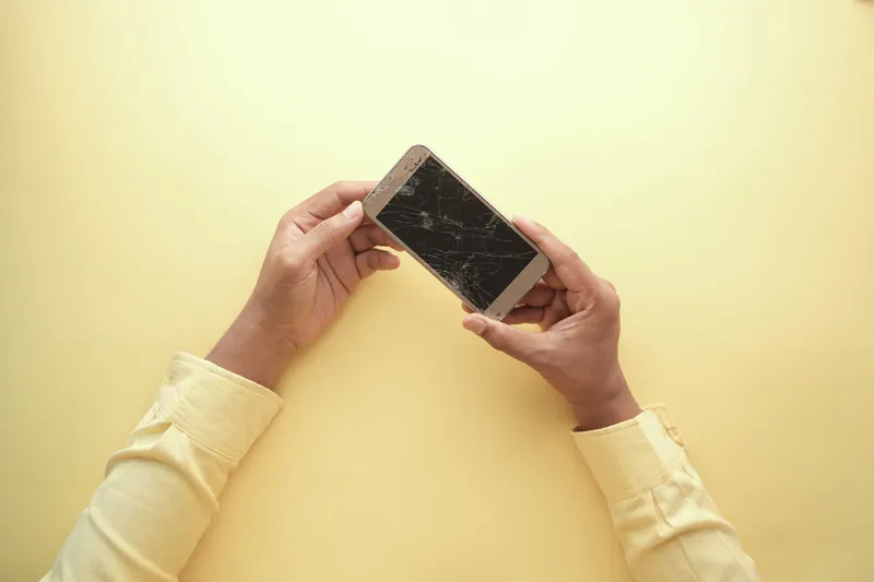 To hender holder en mobiltelefon med knust skjerm