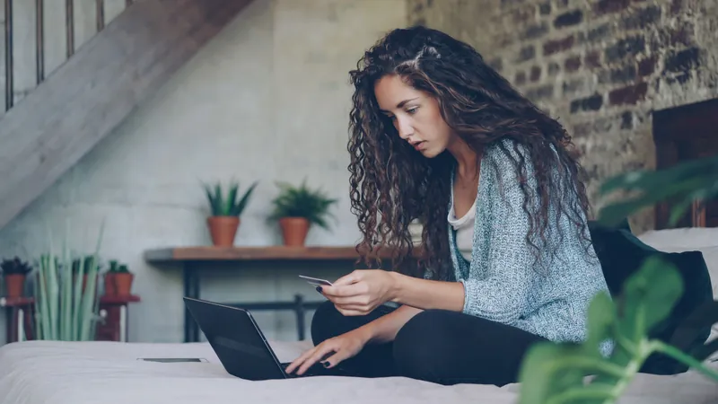 En person sitter med en laptop og holder et betalingskort i hånden