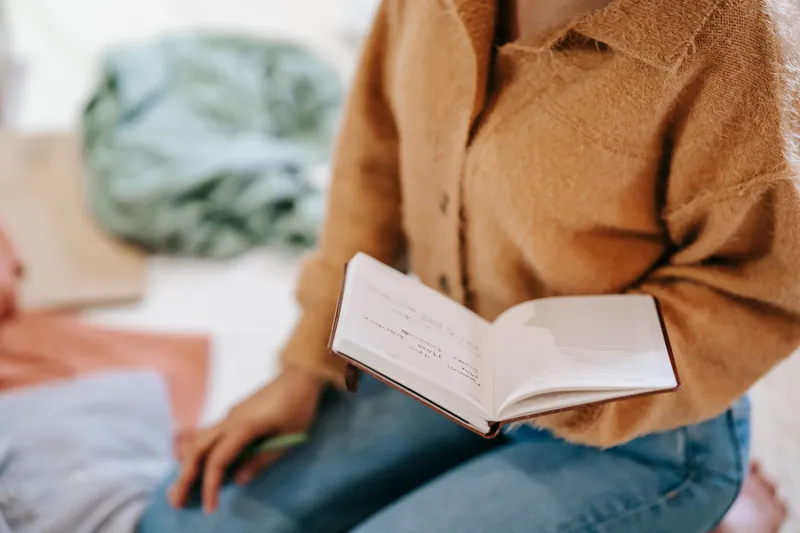 En person sitter på gulvet og leser i en åpen notatbok