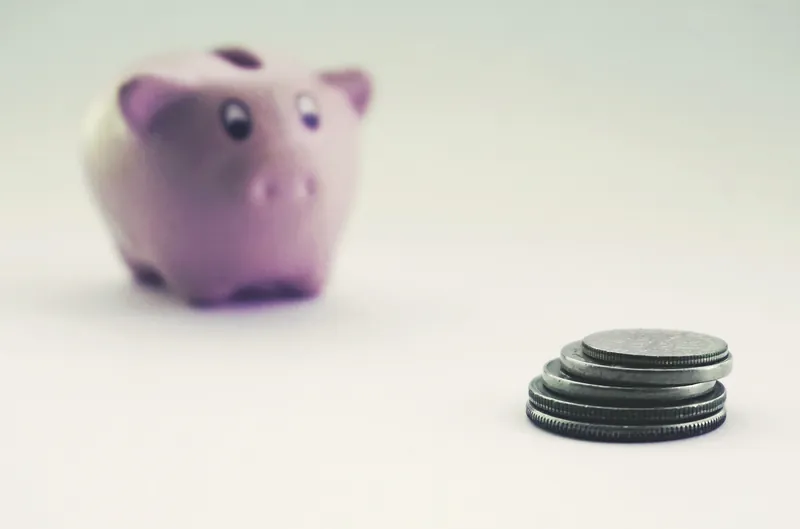 En liten stabel mynter i fokus, med en rosa sparegris ute av fokus i bakgrunnen
