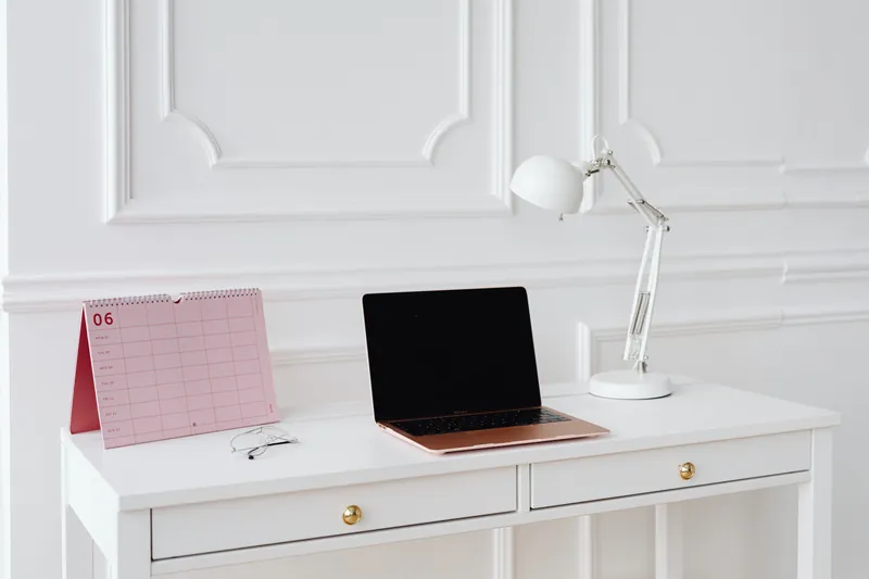 Et ryddig skrivebord med laptop, bordkalender og lampe