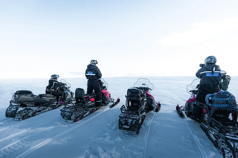 Fire snøscootere med førere på en snøslette på Svalbard